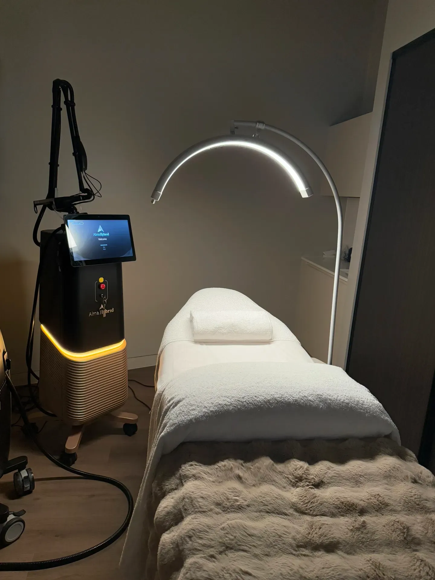 Treatment room: Bed with white linens, light fixture, and laser machine.