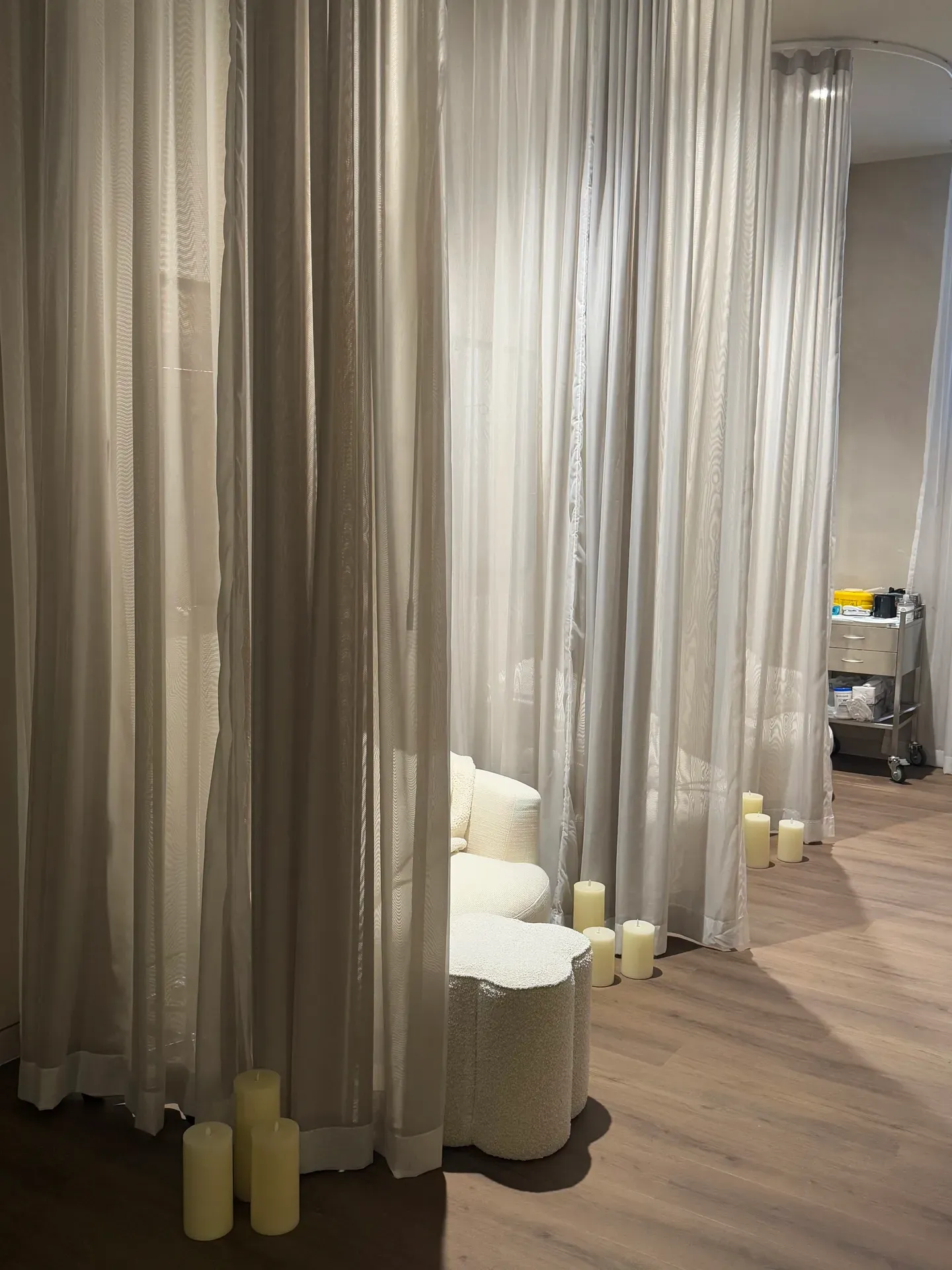 Cozy room with draped white curtains, a small couch, candles, and a medical cart.
