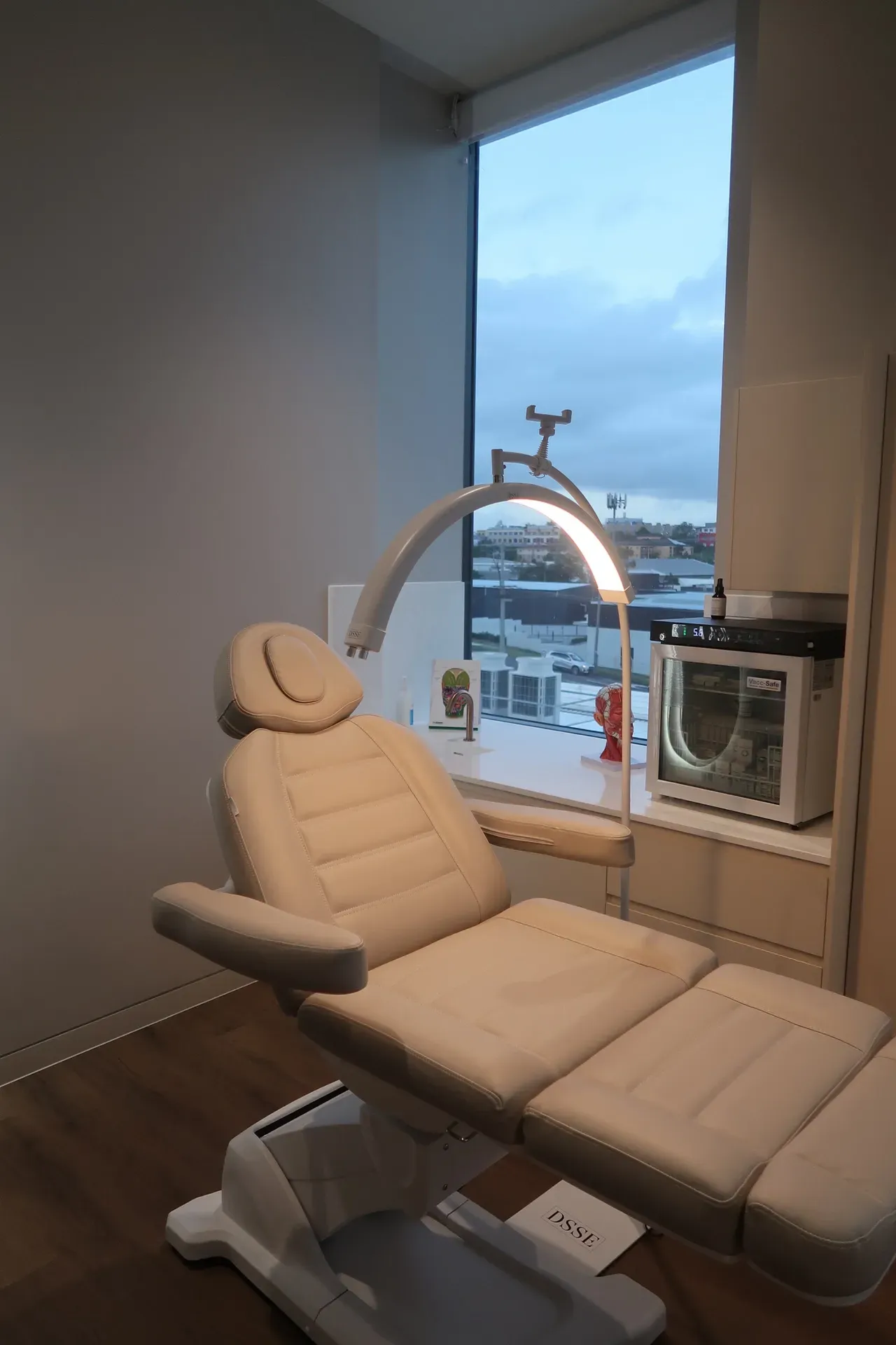 Medical chair in a room with a large window, a lamp, and small medical equipment.