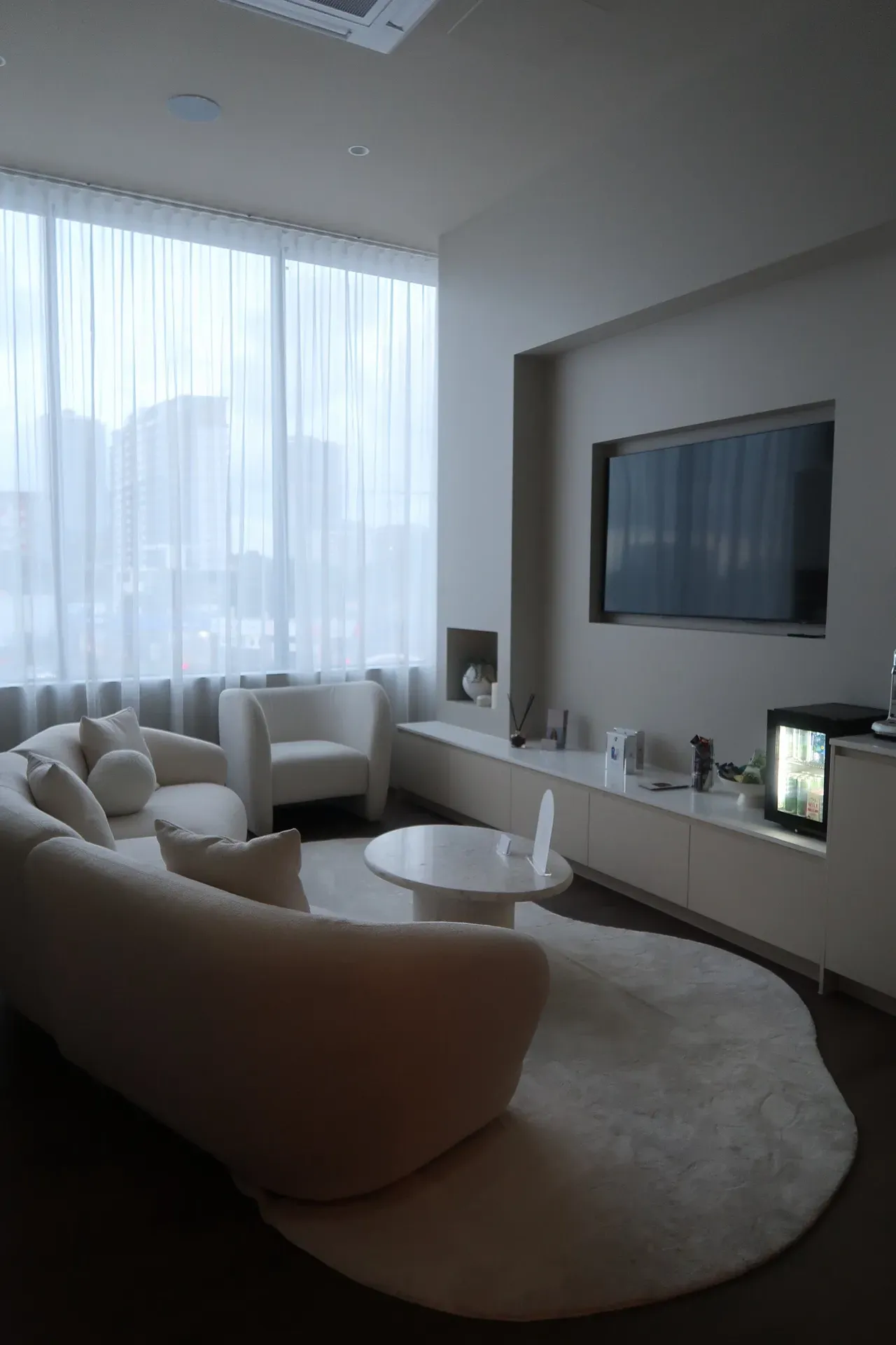 A bright, modern living room with curved sofa, white rug, and large window.