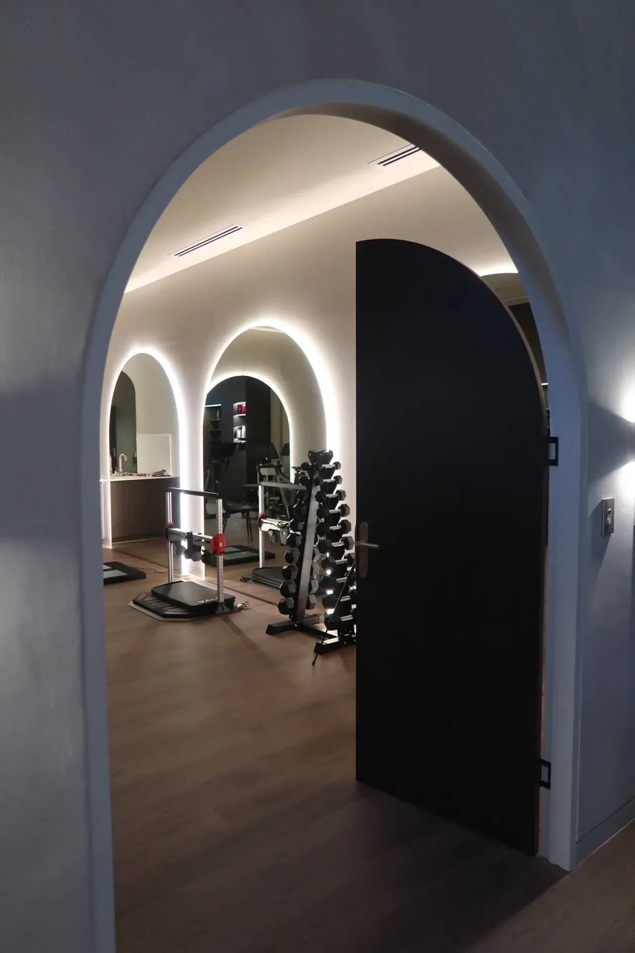Archway opening to a home gym with fitness equipment, brown flooring, and curved walls.