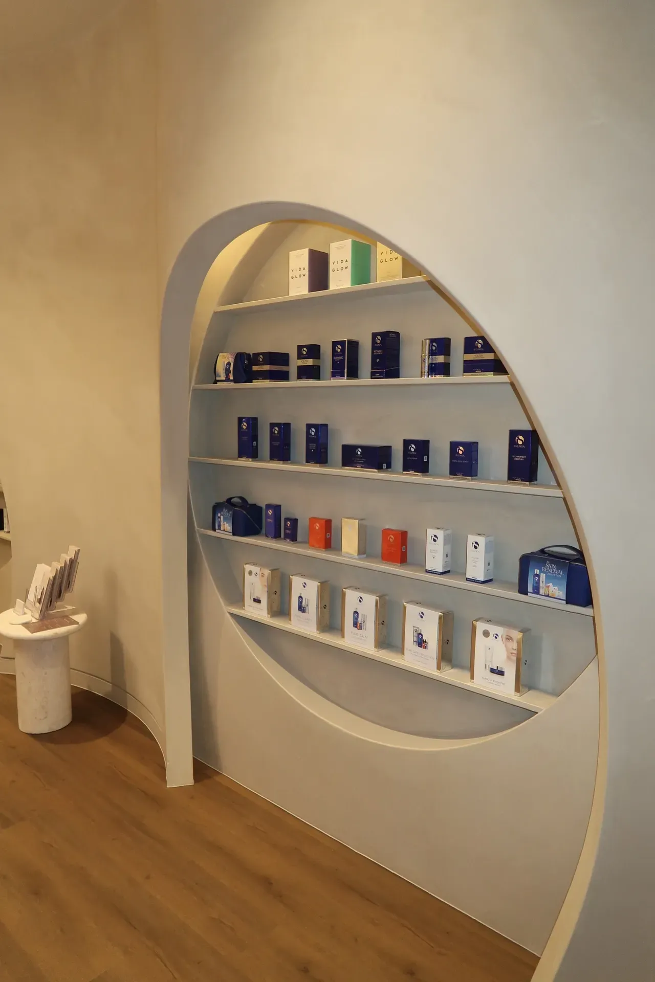 Shelves in an alcove display products, including boxes and other items, in a store with wood flooring and white walls.
