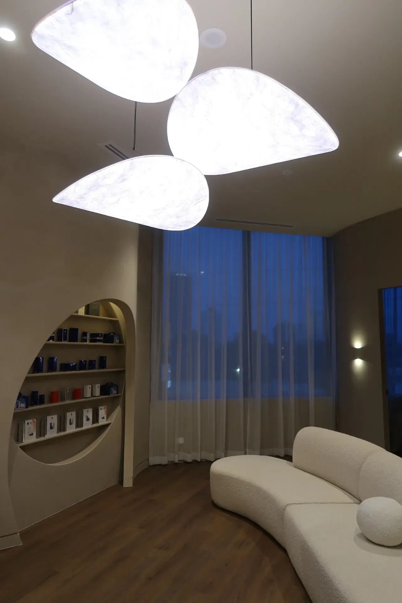 Modern room with curved white sofa, teardrop-shaped lights, and window with sheer curtains.