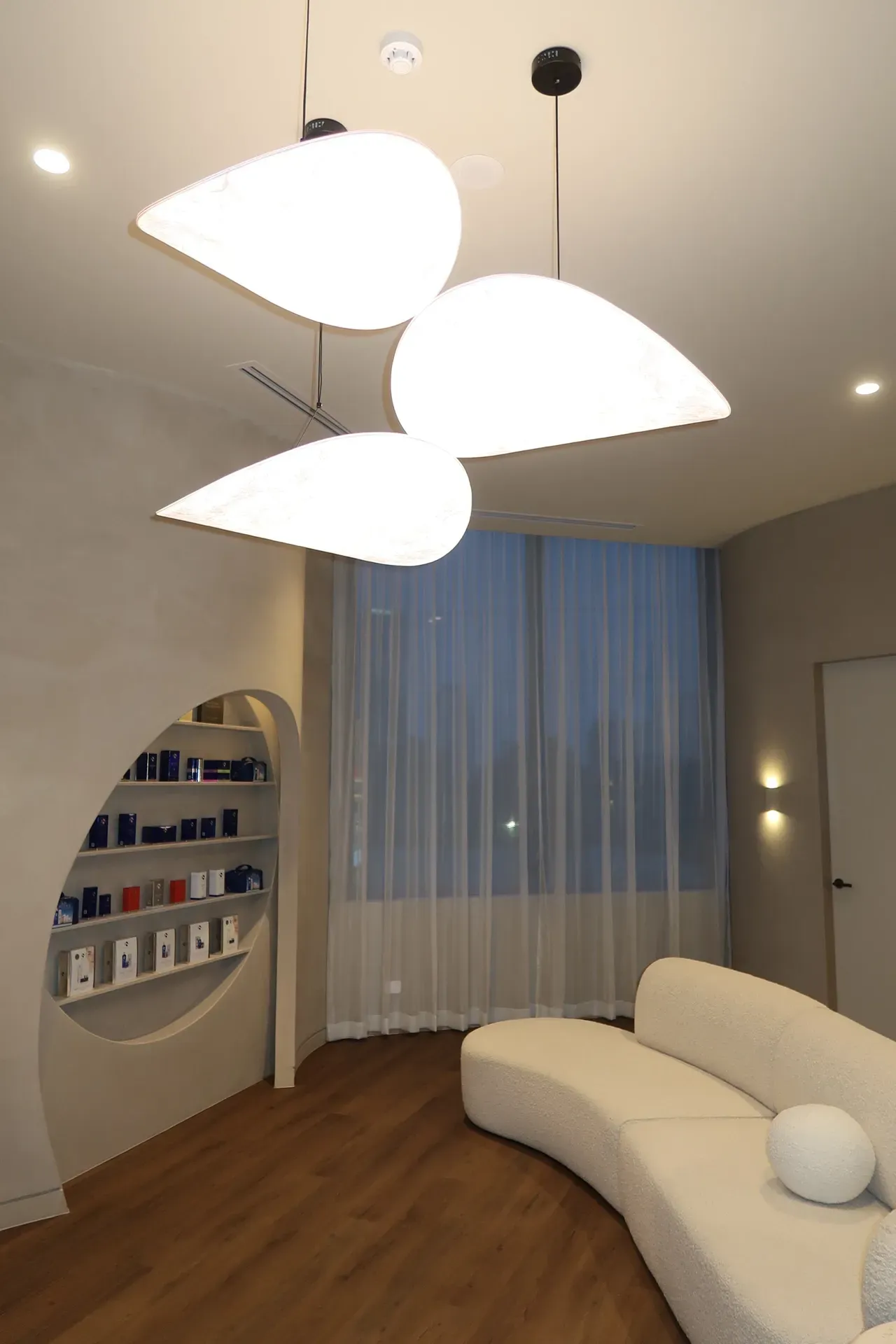 Interior of a spa with petal-shaped pendant lights, curved white couch, and products displayed in a rounded alcove.