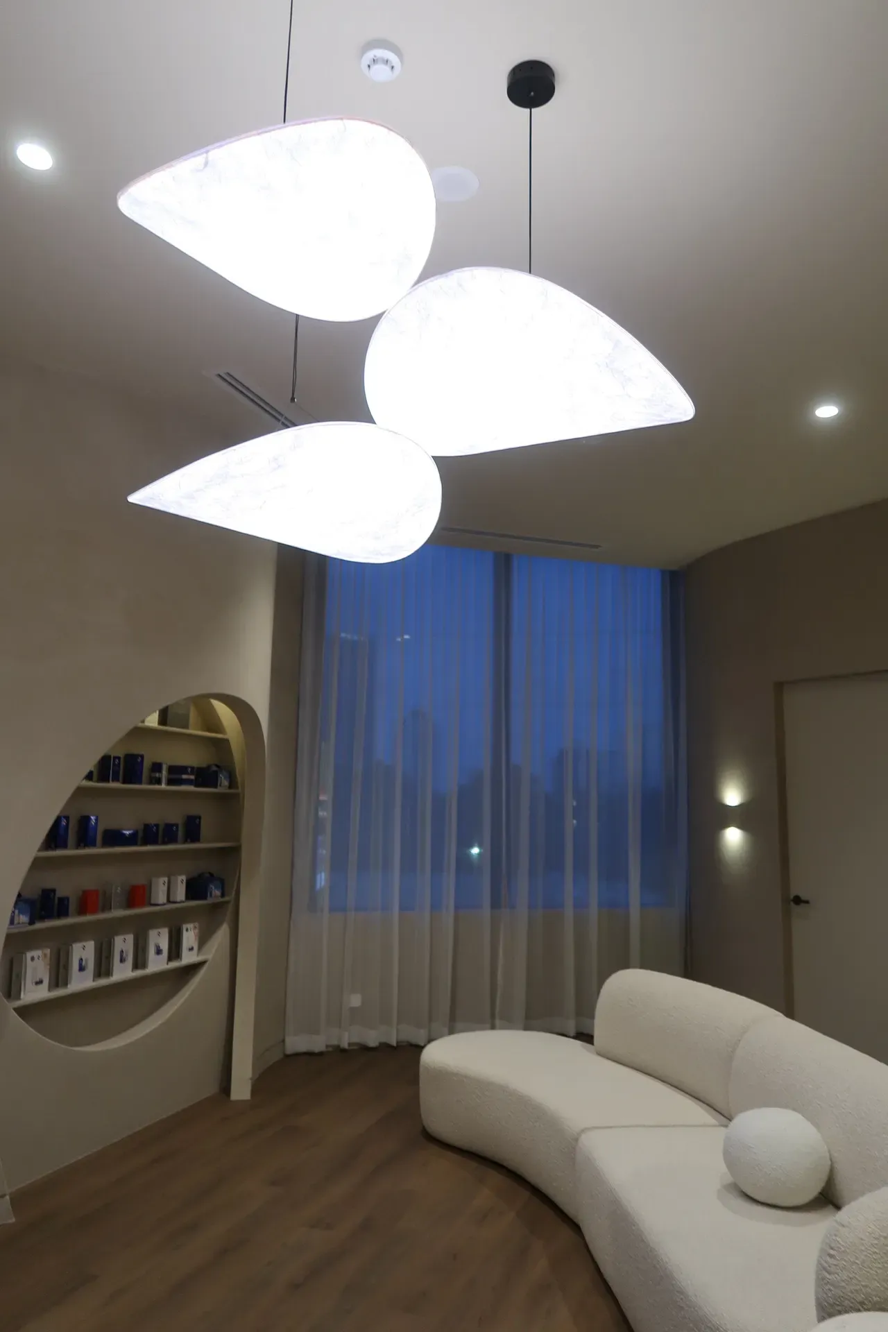Modern waiting room with curved white sofa, pendant lights, and a display niche.