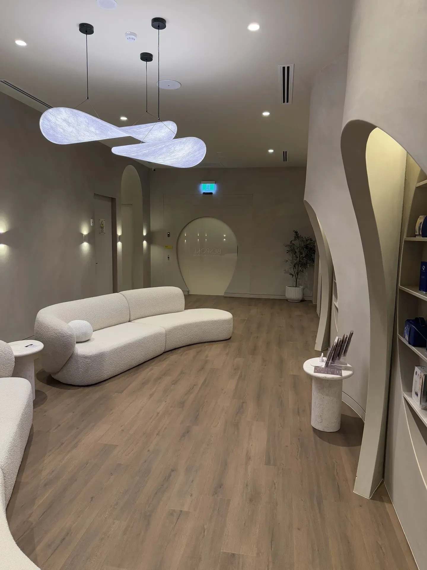 Modern waiting area with white curved sofa, wooden floor, and decorative lighting.
