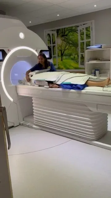 Woman assisting a patient on an MRI machine. Blue and white colors. Brightly lit room.