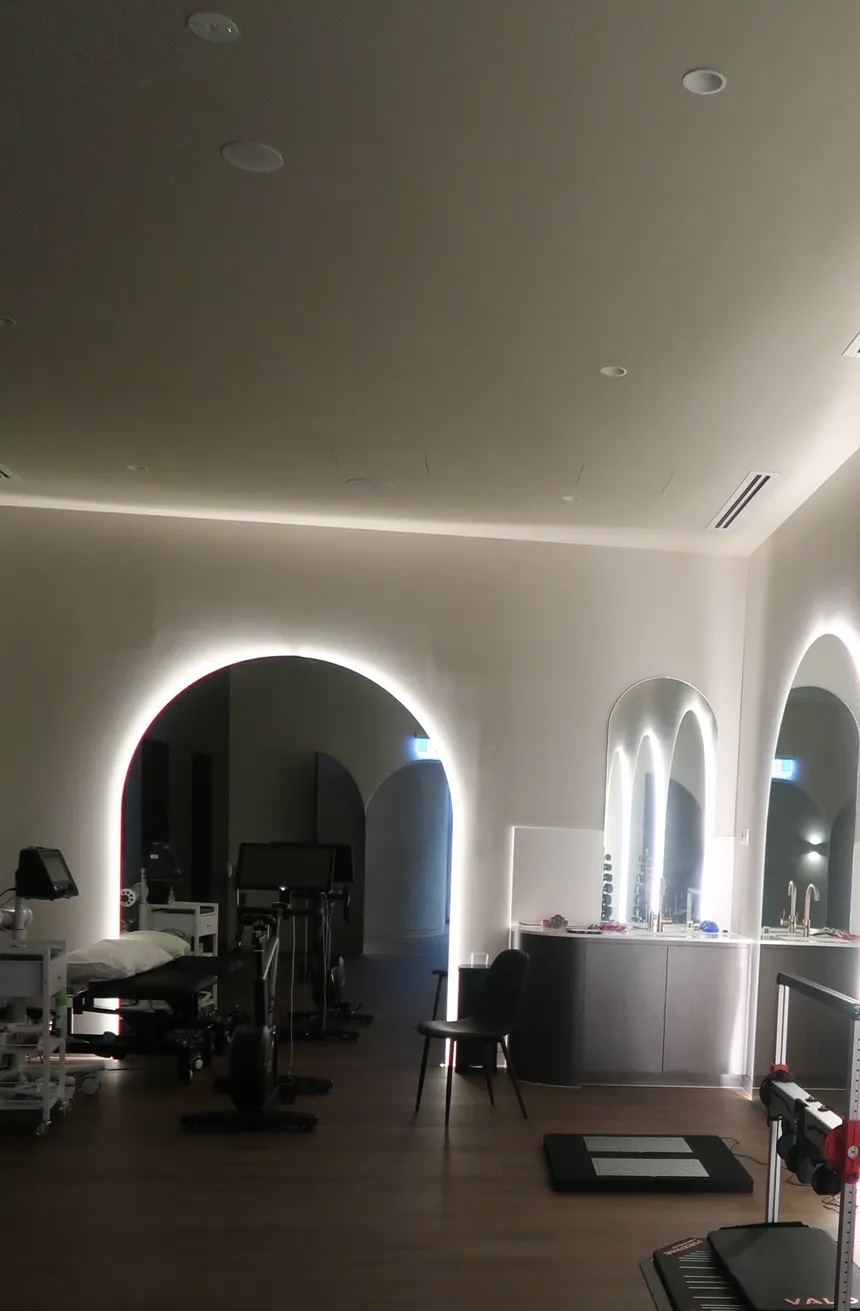 Interior view of a modern workout or therapy room with arched doorways and mirrors, lit with soft white lights.