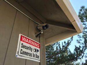 A security camera is mounted on the side of a building next to a warning sign.
