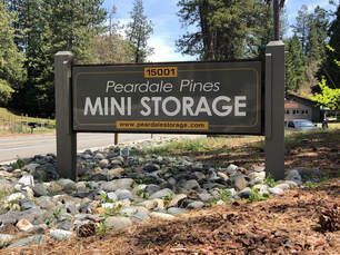A sign for peardale pines mini storage is sitting on top of a pile of rocks.