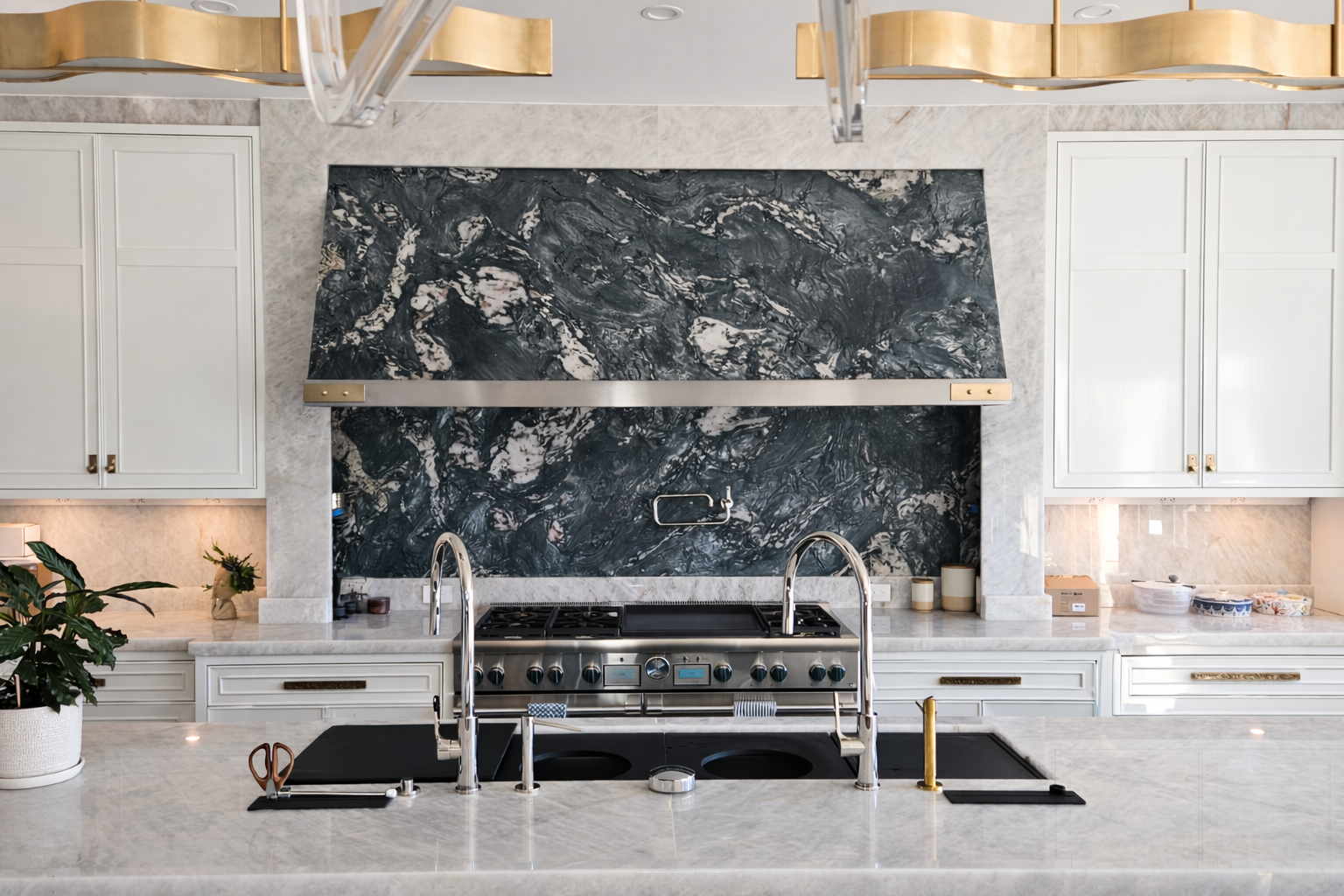 Luxurious kitchen with white cabinets, dark marble backsplash, gold light fixtures, and a large island.