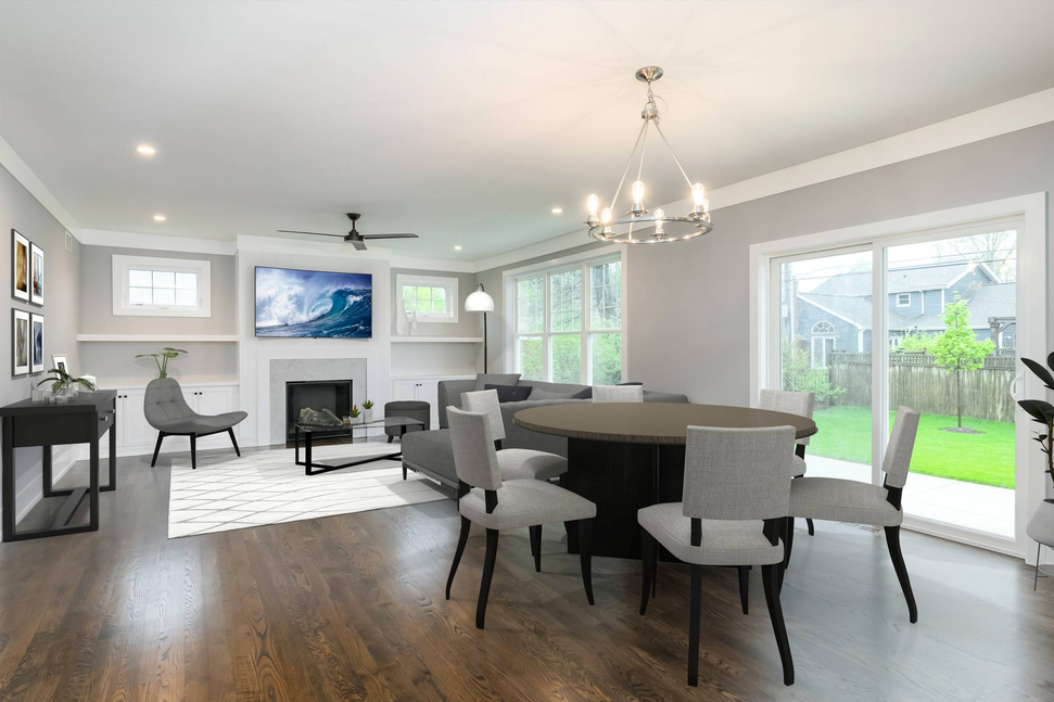 Open-concept living room and dining area, featuring a fireplace, large windows, dining table with chairs, and hardwood floors.