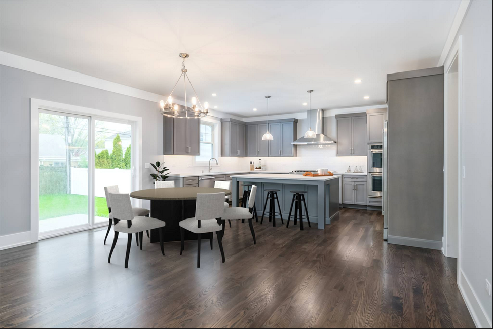 Modern kitchen with gray cabinets, island with stools, round dining table, and sliding glass doors.
