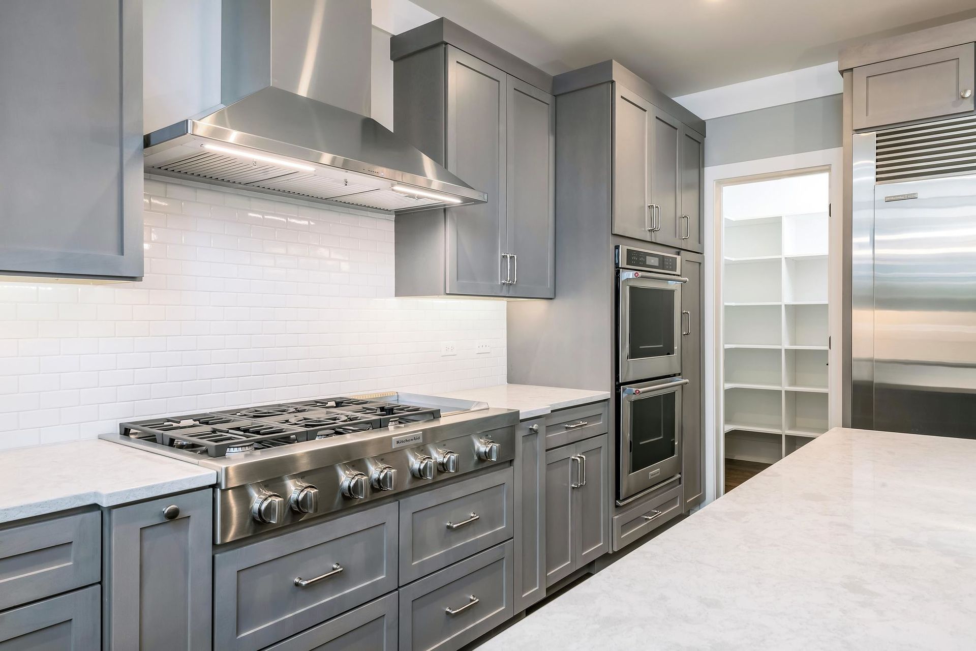 Gray kitchen with stainless steel appliances, white countertops, and a pantry.