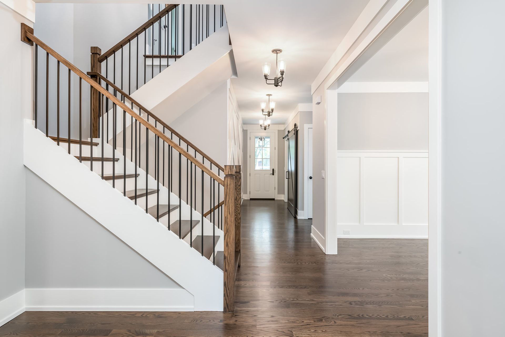A bright entryway with a staircase, dark wood floors, and light gray walls.