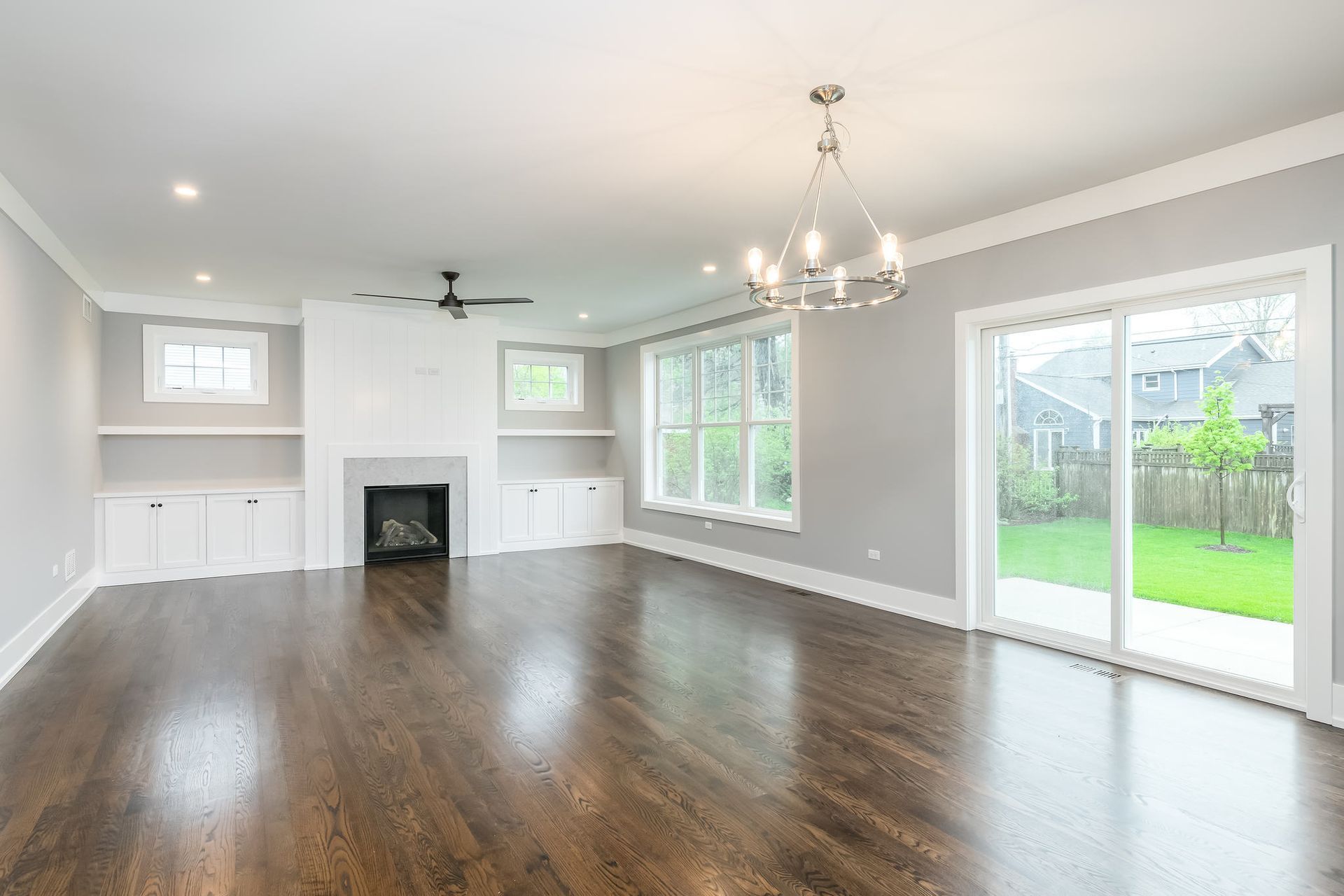 Spacious living room with dark wood floors, fireplace, and large windows overlooking a green lawn.