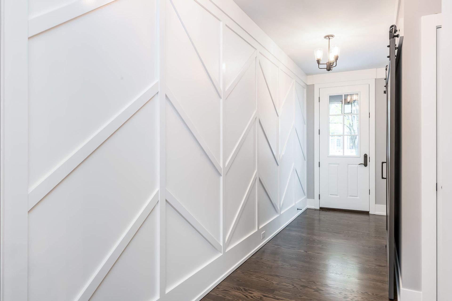 White geometric accent wall in hallway, leading to a white door with a glass panel.