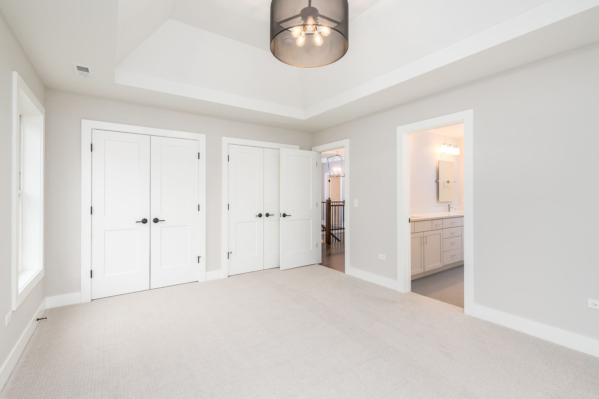 Empty bedroom with white doors, gray walls, beige carpet, and a view into a bathroom.