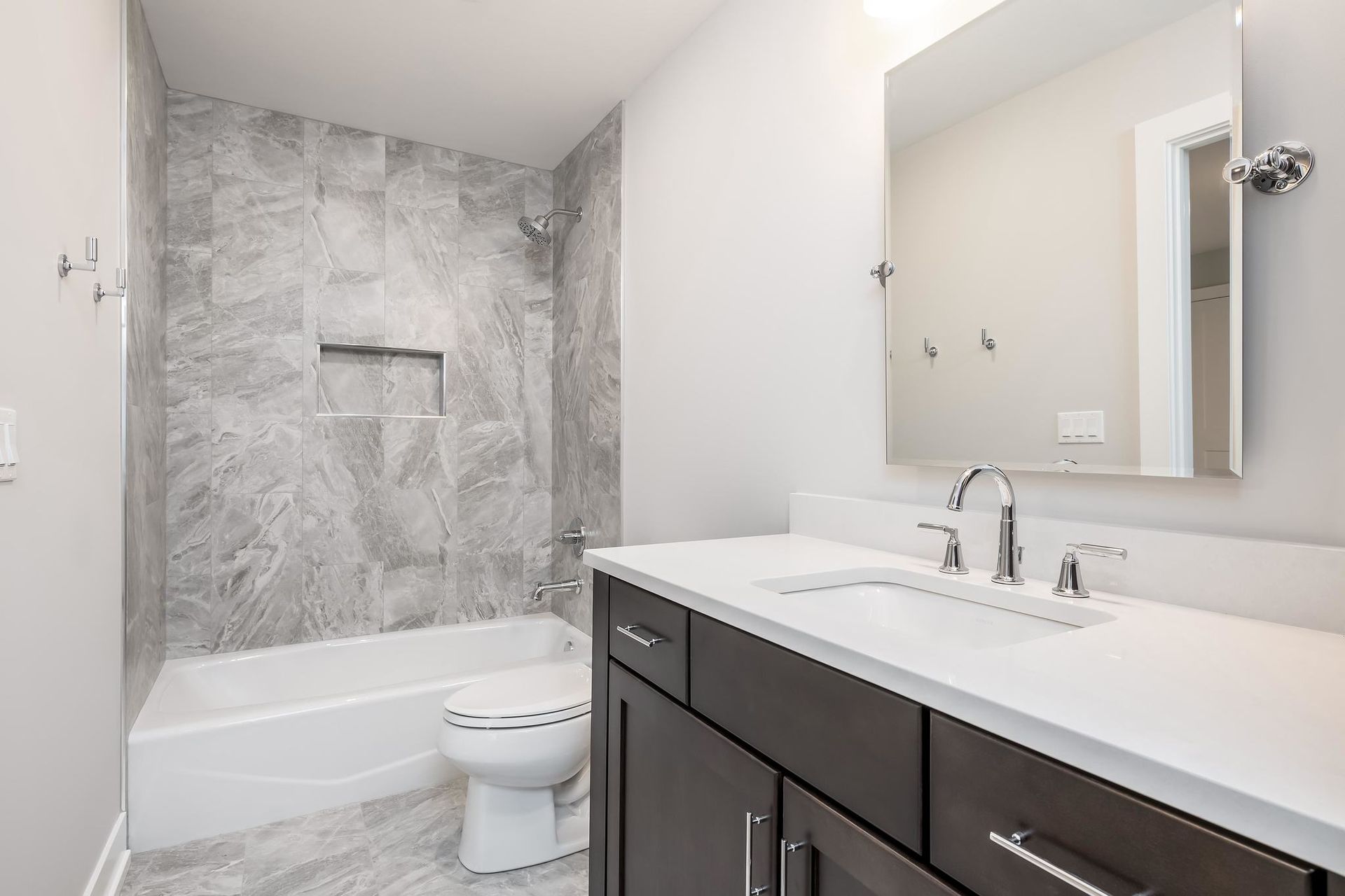 Modern bathroom with gray marble shower tiles, dark wood vanity, and white countertop.