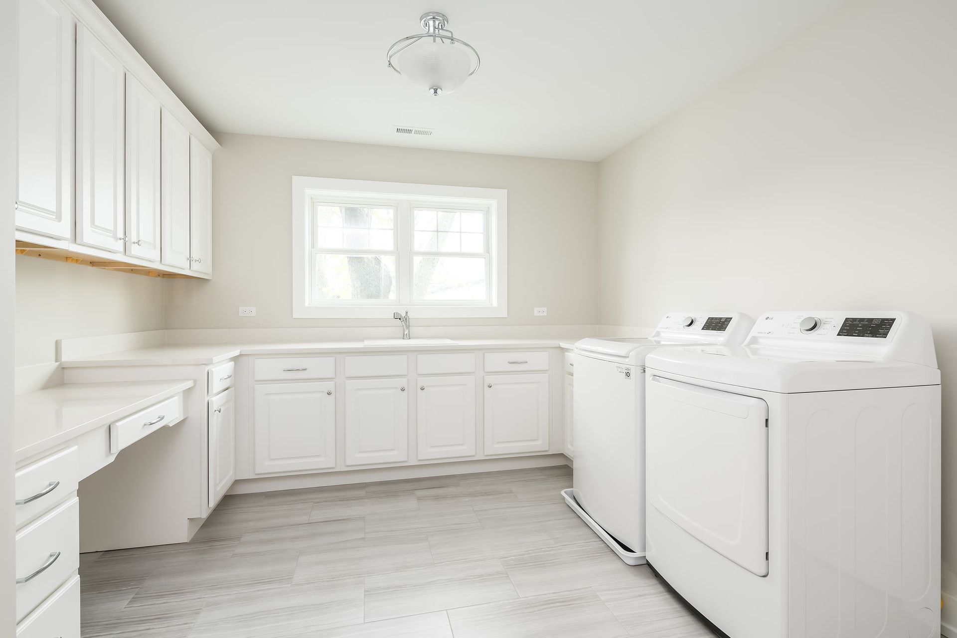 A bright, white laundry room with cabinets, a sink, and a washer and dryer.