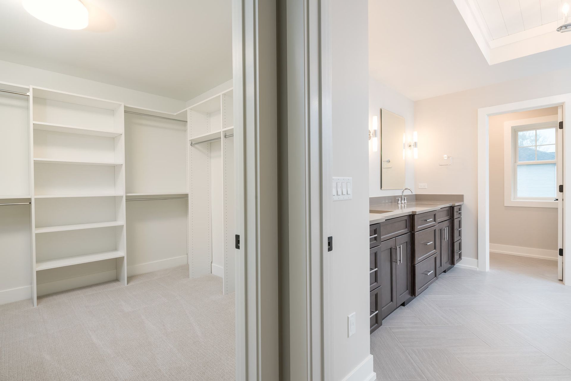 Walk-in closet with built-in shelving, connected to a bathroom with a vanity and window.