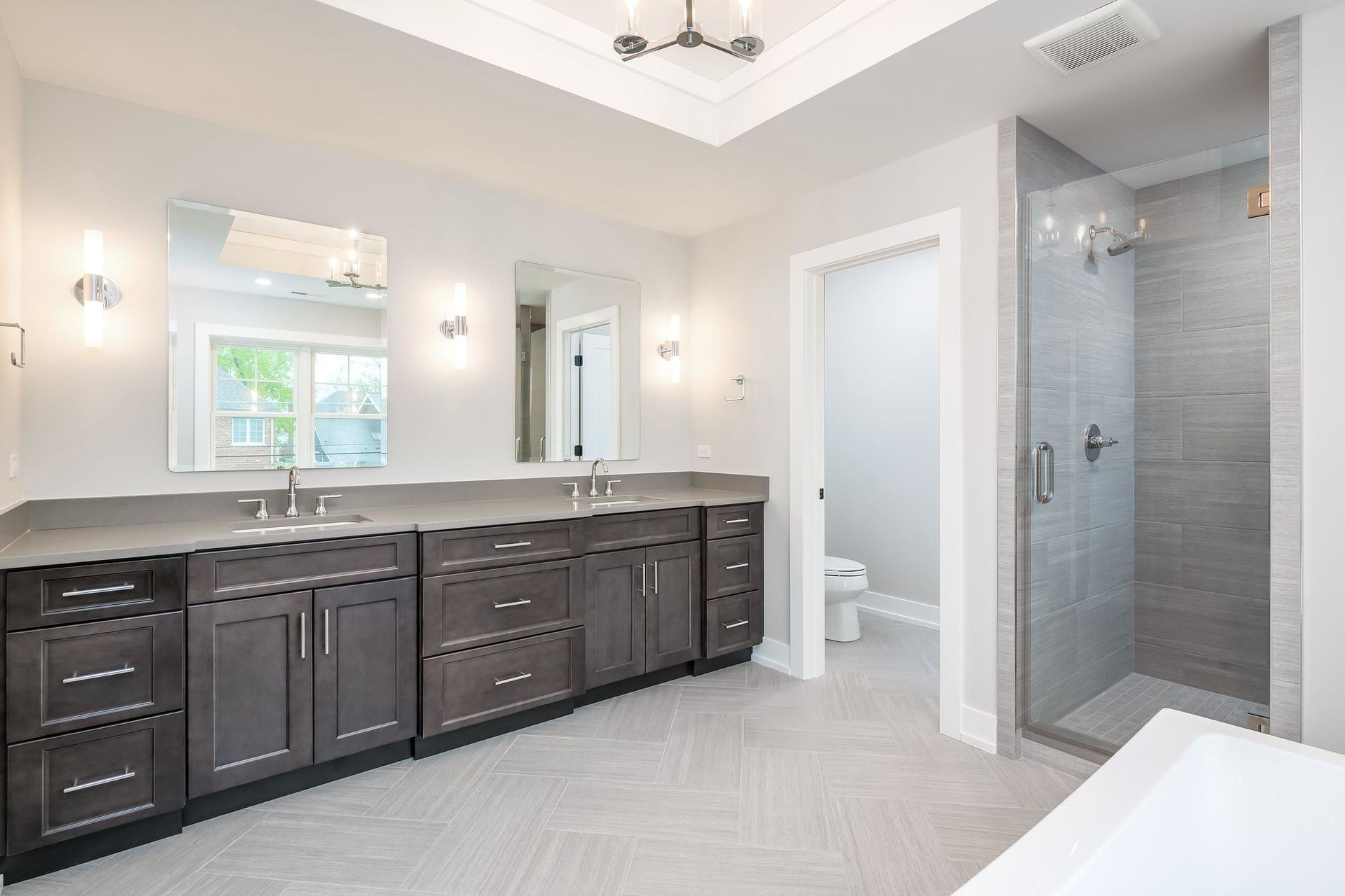 Modern bathroom with dark cabinets, grey countertops, glass shower, and large mirrors.