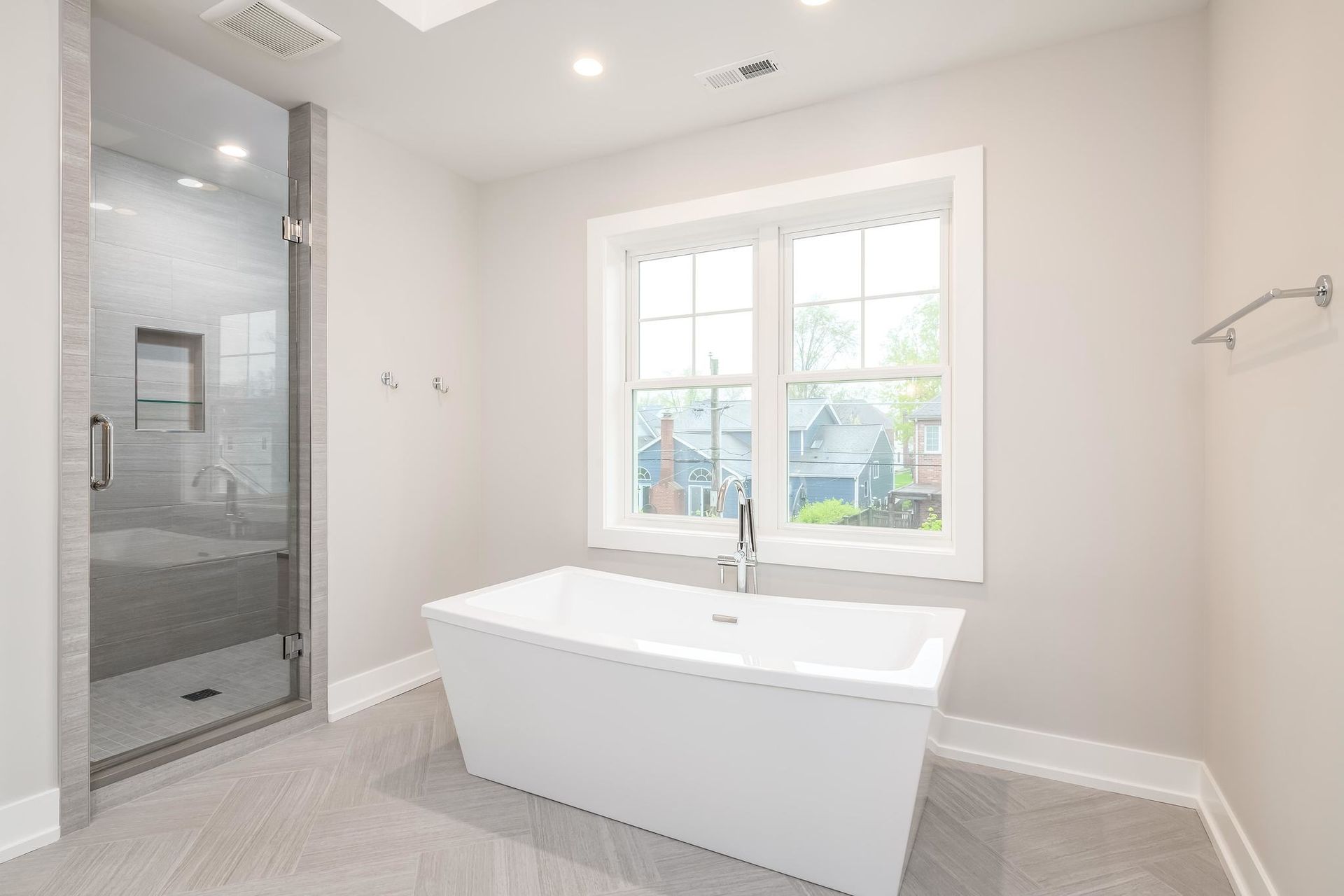 Modern bathroom with a white freestanding tub, a glass shower, and a large window.