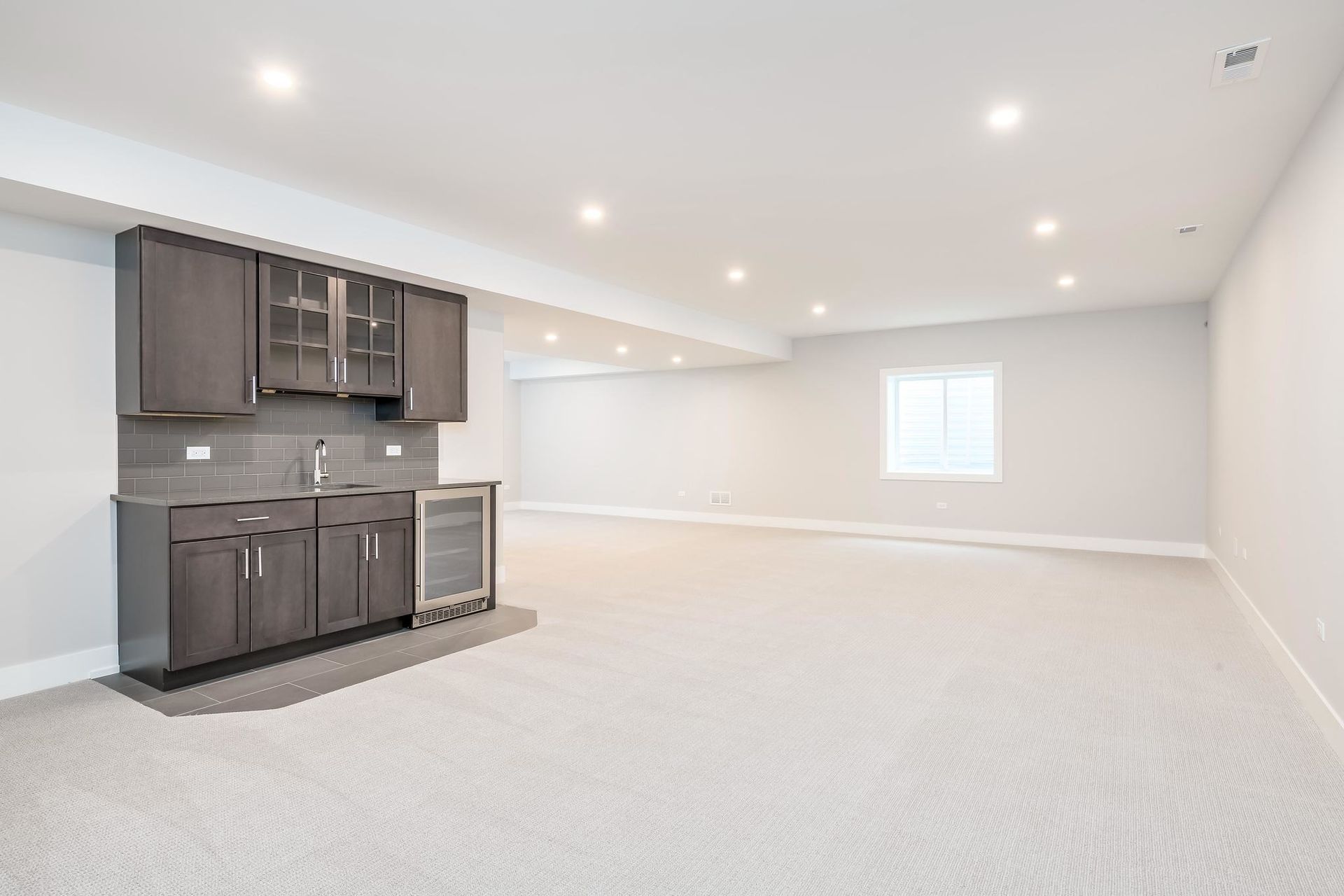 Empty basement with built-in bar featuring dark cabinets, a sink, and a small refrigerator.