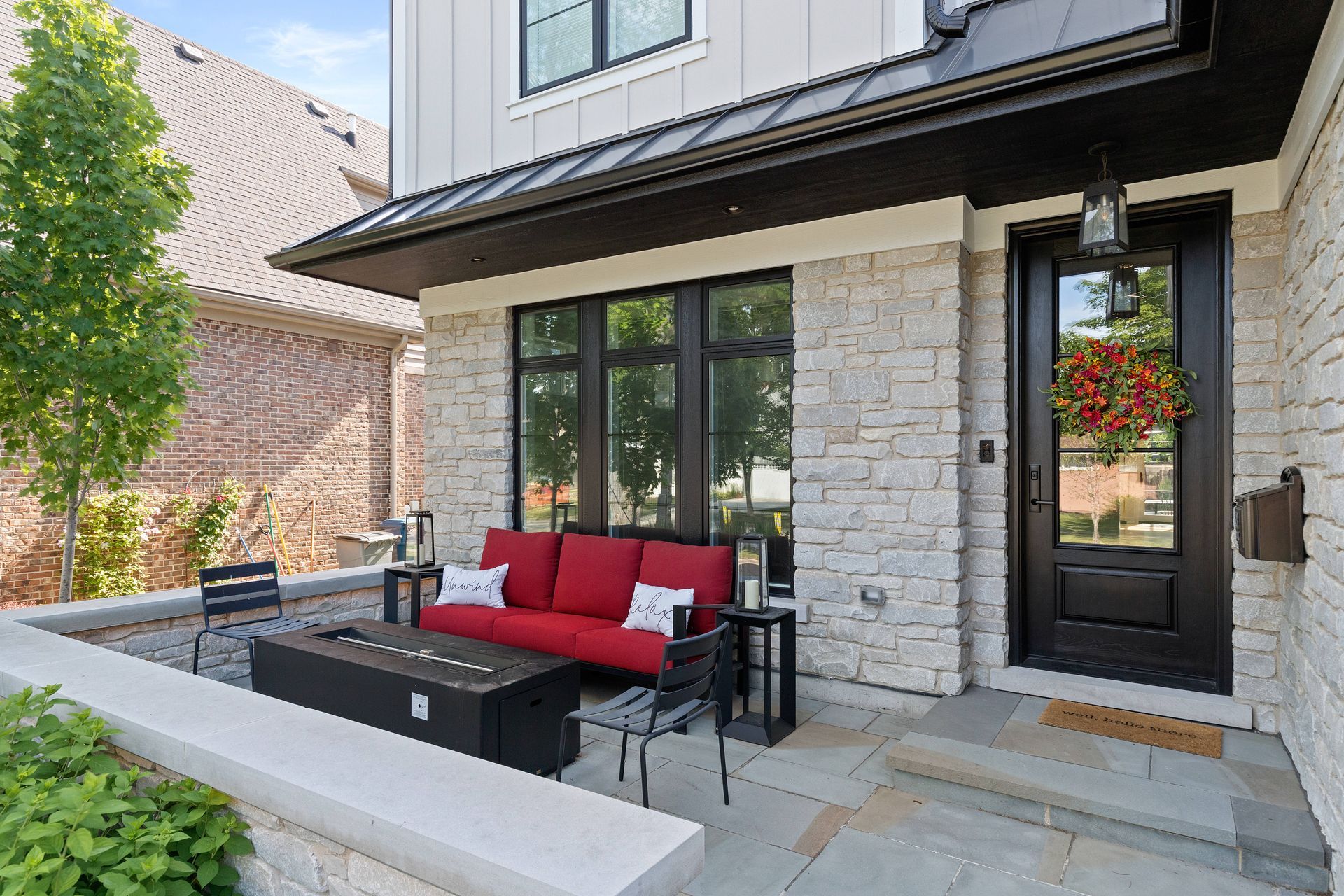 Modern home exterior with red couch on patio, fire pit, black door, and stone facade.