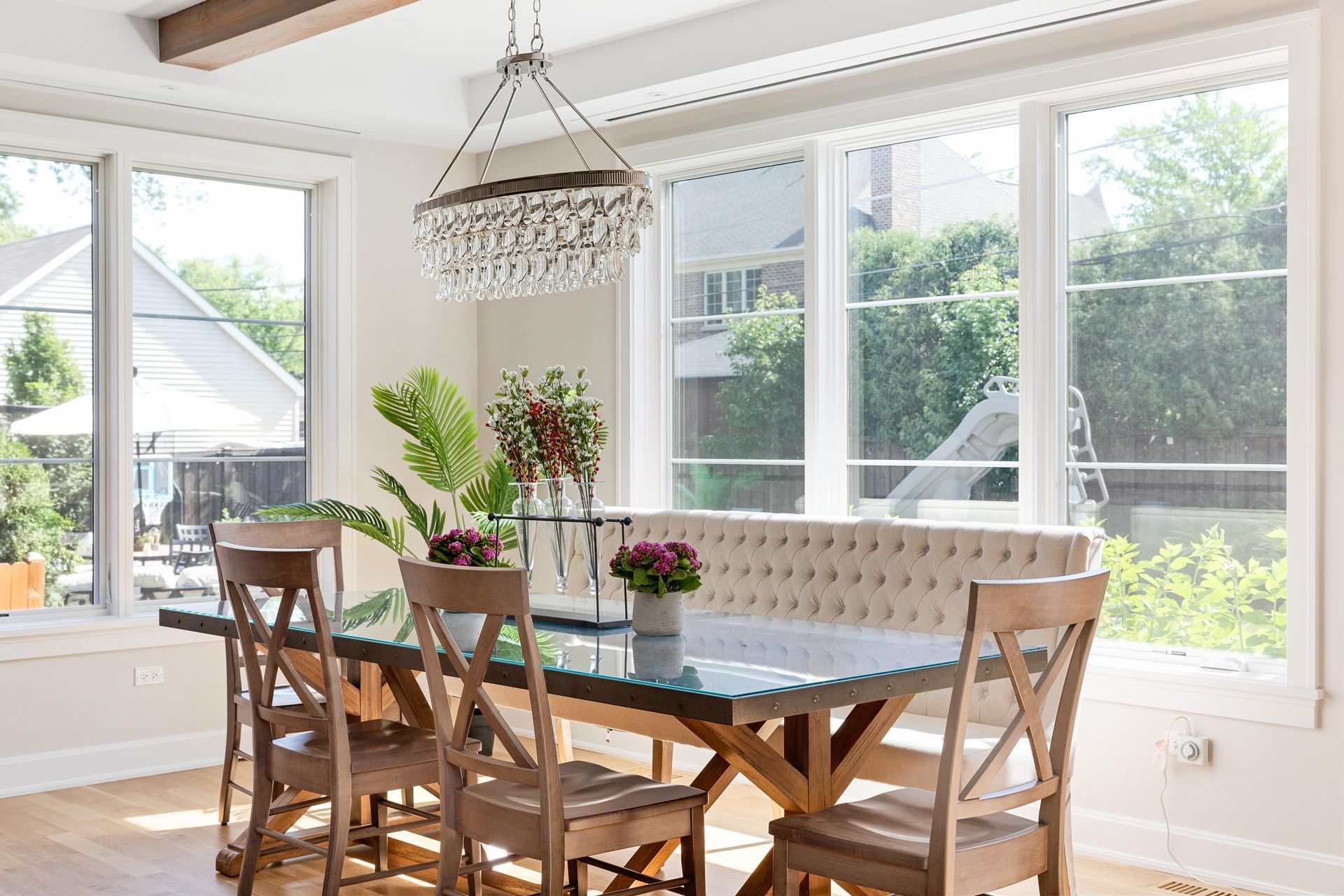 Dining room with a table, chairs, bench seating, and a chandelier. Large windows offer a bright view.