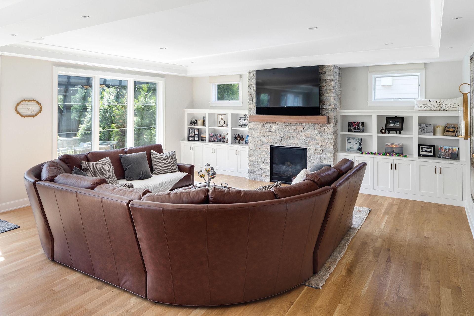 A living room with a large brown sectional sofa, fireplace, built-in shelves, and large windows.