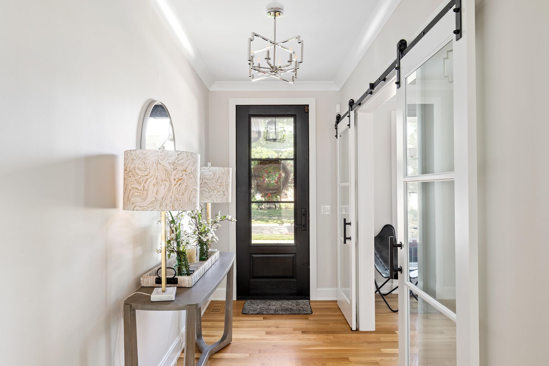 Narrow hallway with a gray console table, black door, and light wood floors.