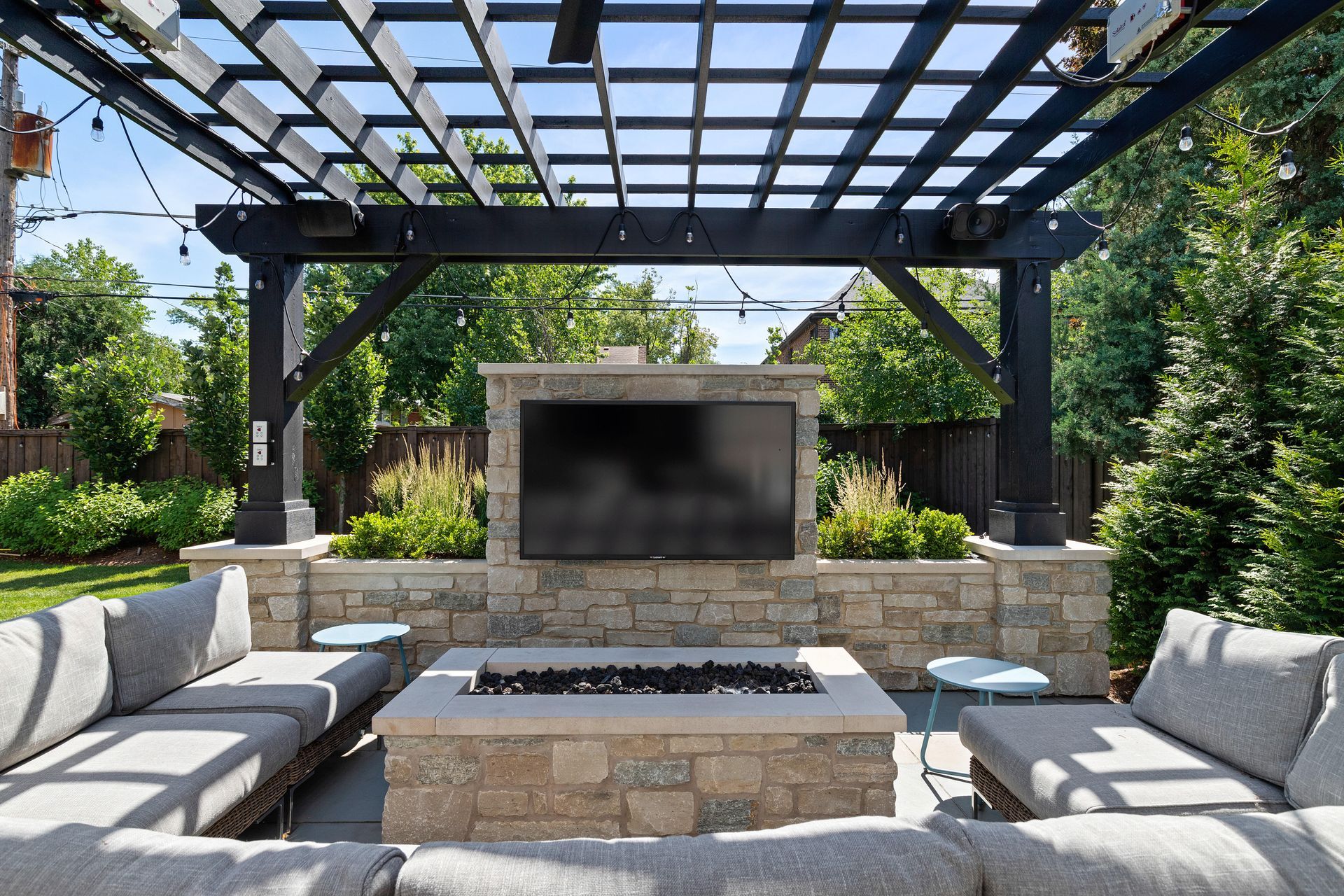 Outdoor living space with a stone fire pit, sectional sofa, large TV, and pergola.