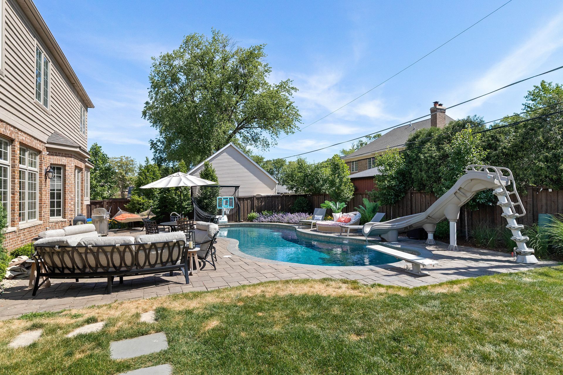 Backyard with a swimming pool, lounge furniture, and a water slide on a sunny day.