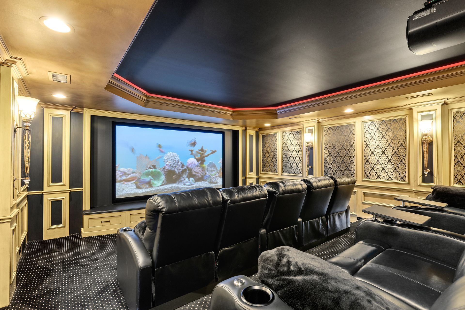 Luxury home theater with black reclining seats facing a large screen, gold accents, and ornate details.