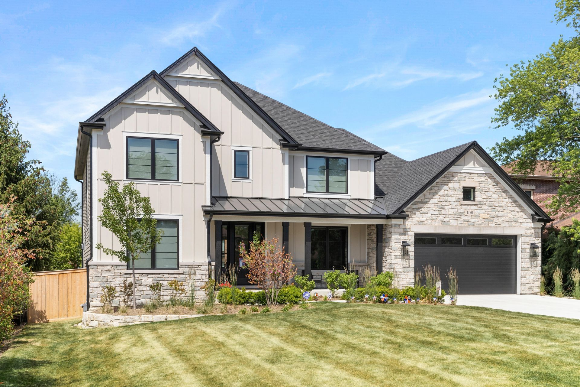 Two-story house with stone accents and dark roof, gray and white siding, and a well-kept lawn.