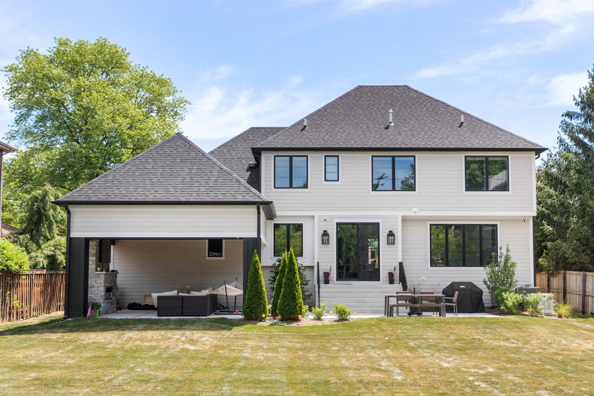 White two-story house with black-framed windows and a covered patio with outdoor seating.
