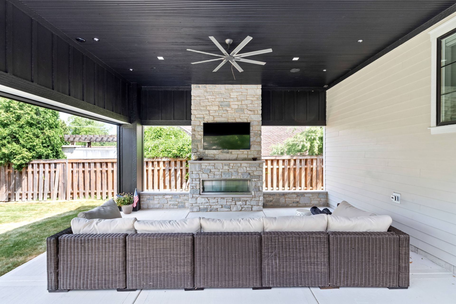 Covered patio with fireplace, TV, sectional sofa, and ceiling fan.
