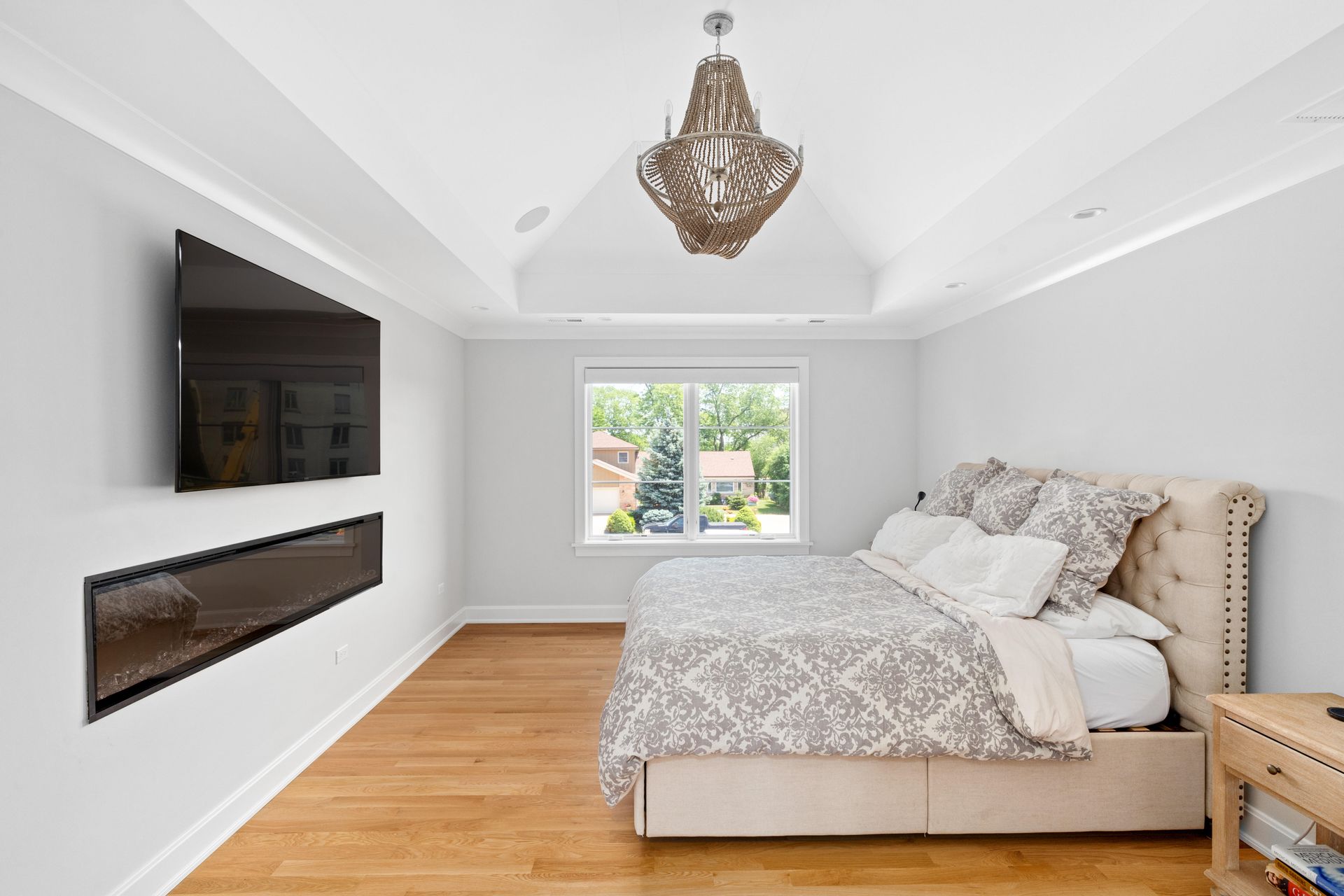 Bedroom with a bed, TV, window, chandelier, and wooden floors.