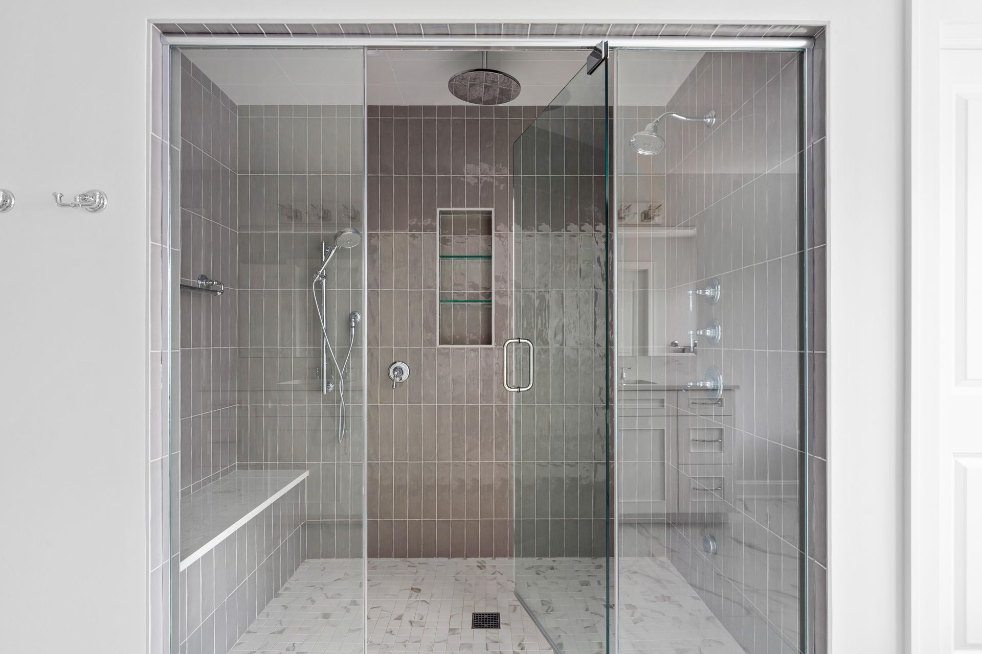 Glass-enclosed shower with bench, shower head, and tiled walls.