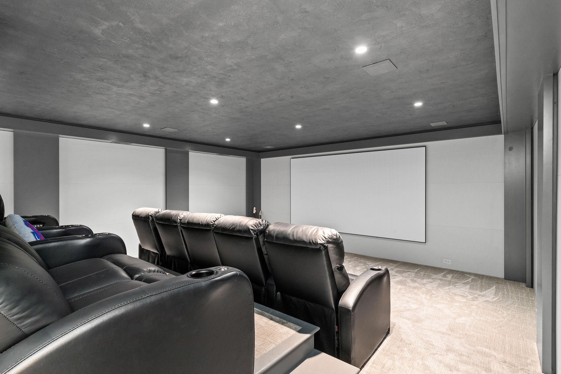 Home theater with black leather reclining seats, screen, and gray walls/ceiling.