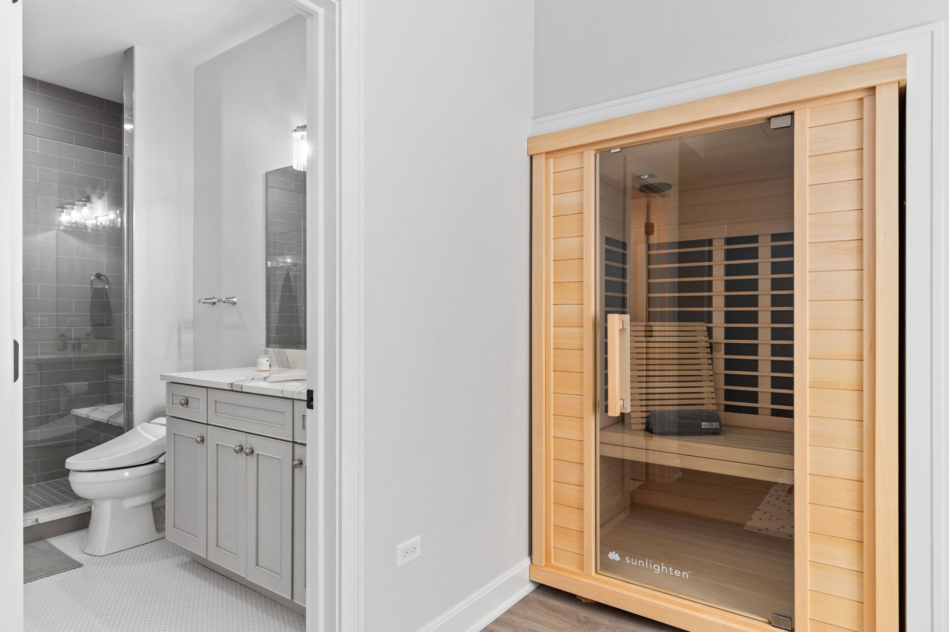 Bathroom with a sauna. Light wood sauna door, gray vanity, shower with dark gray tiles, white toilet.