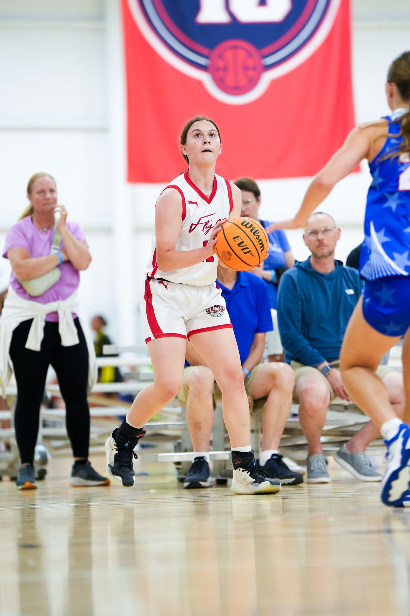 Basketball player in red uniform about to shoot, facing the hoop, with spectators in the background.