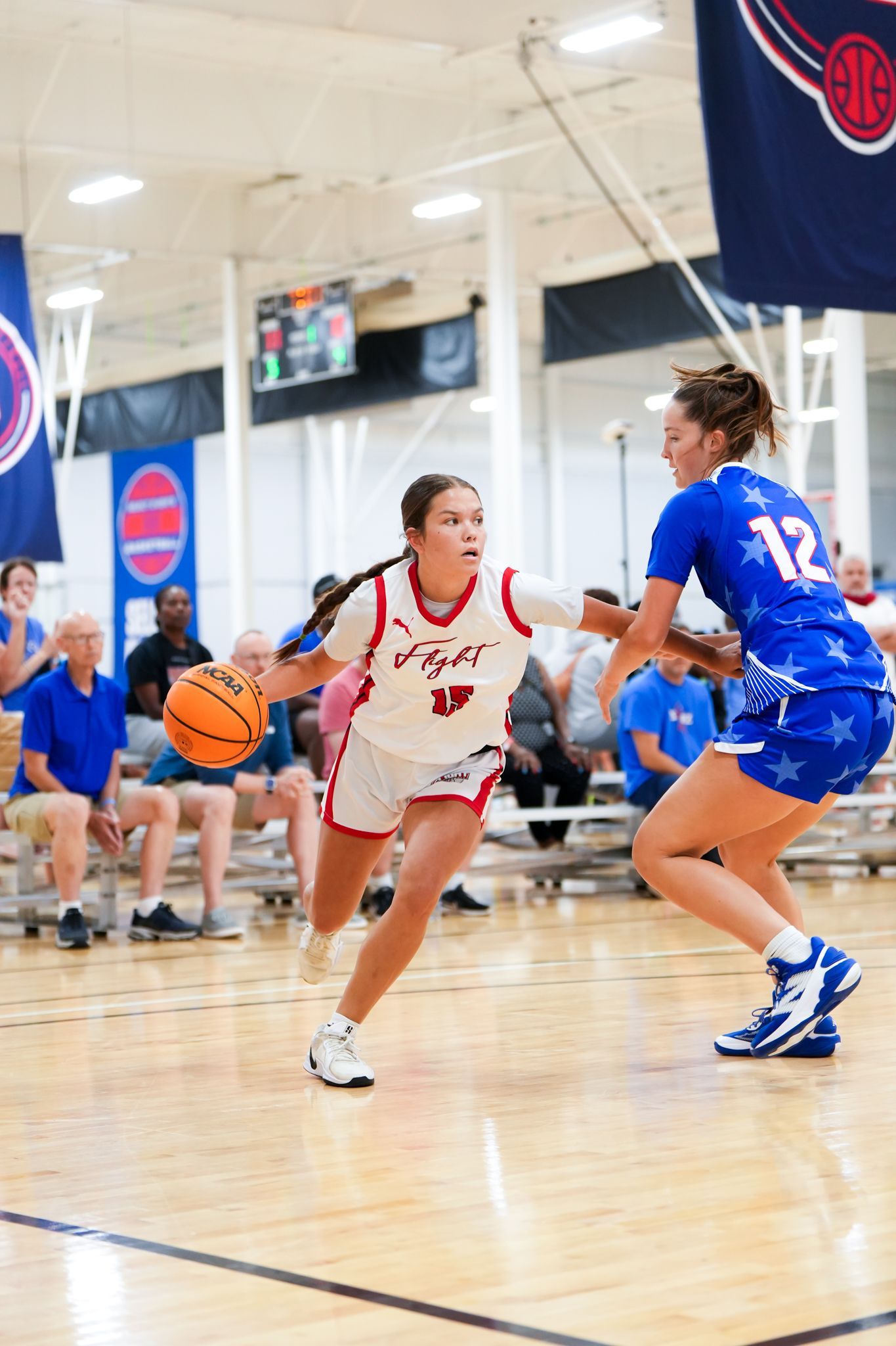 Basketball player in red dribbles past player in blue during a game.