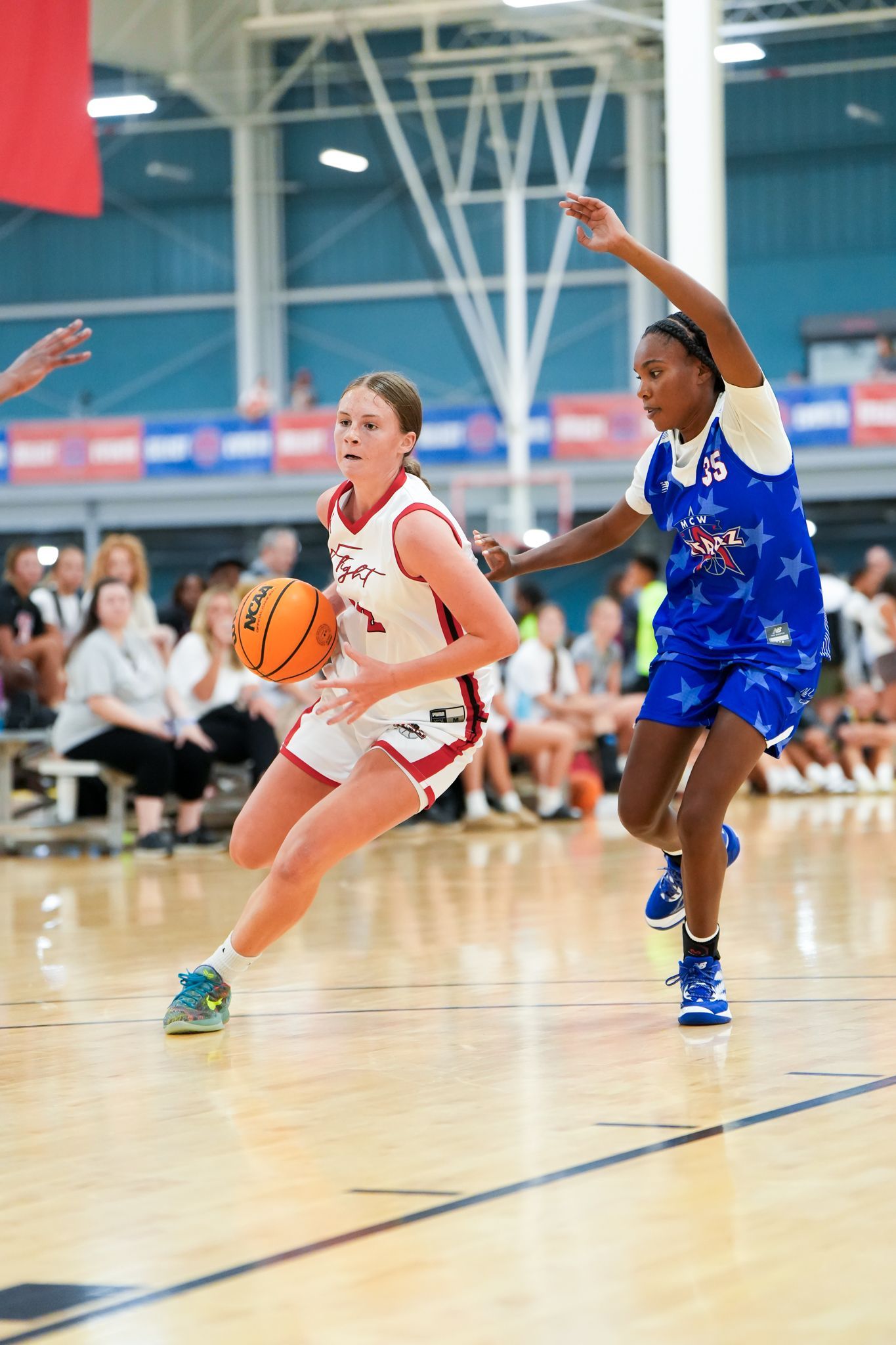 Basketball player in red drives toward the basket, guarded by a player in blue stars on a court.