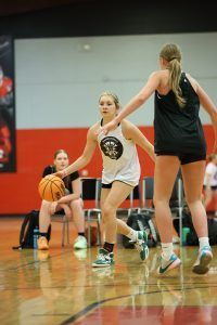Woman dribbles a basketball, guarded by another woman during a practice. A third woman watches.
