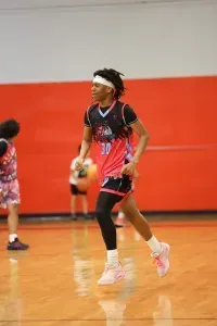 Basketball player in a pink and black jersey runs on a court. He wears a headband and knee sleeve.