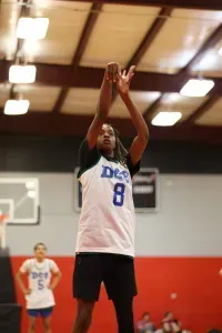 Basketball player in white jersey (number 8) shooting free throw in gym, red and white walls, other players in background.