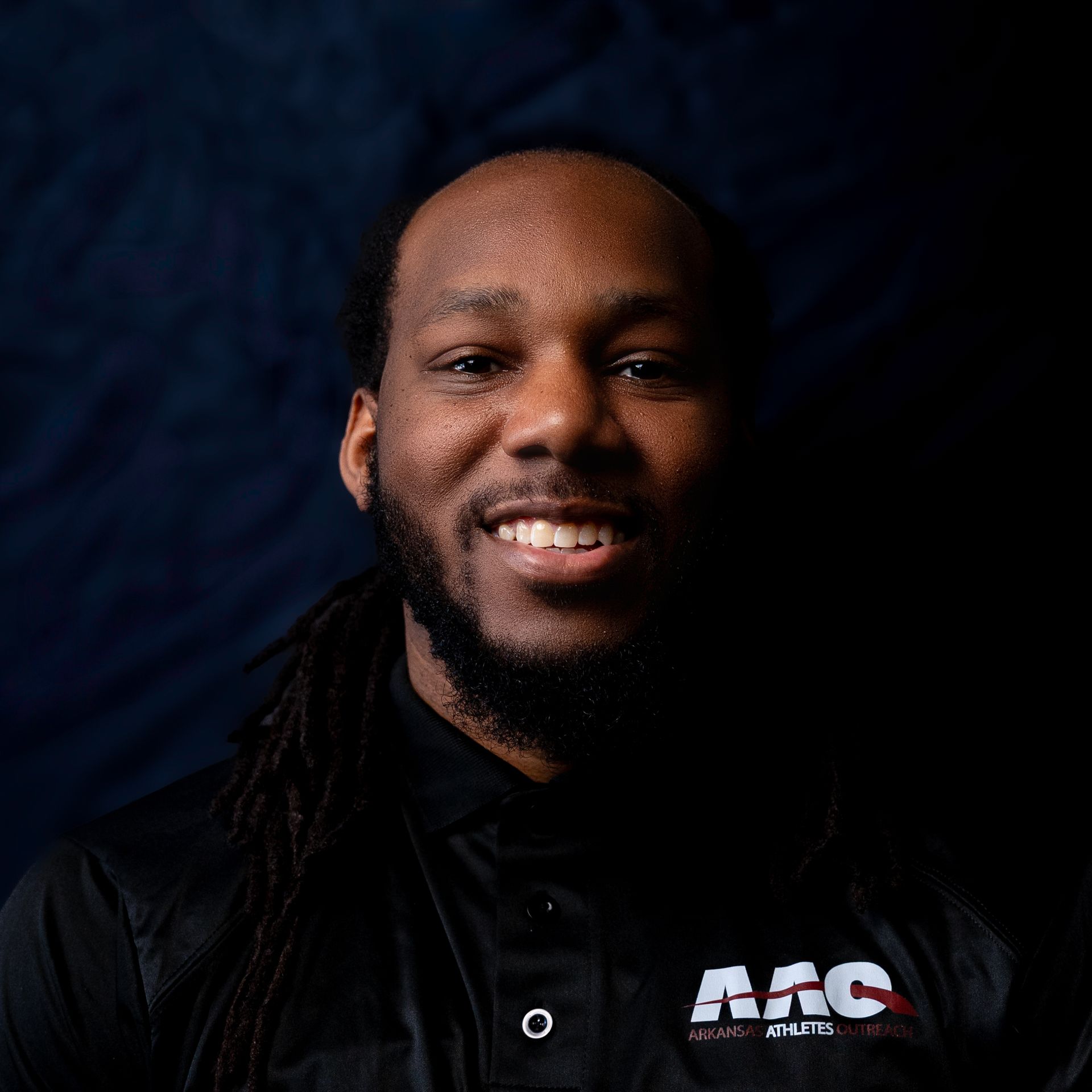 Smiling man in a black shirt against a dark blue background