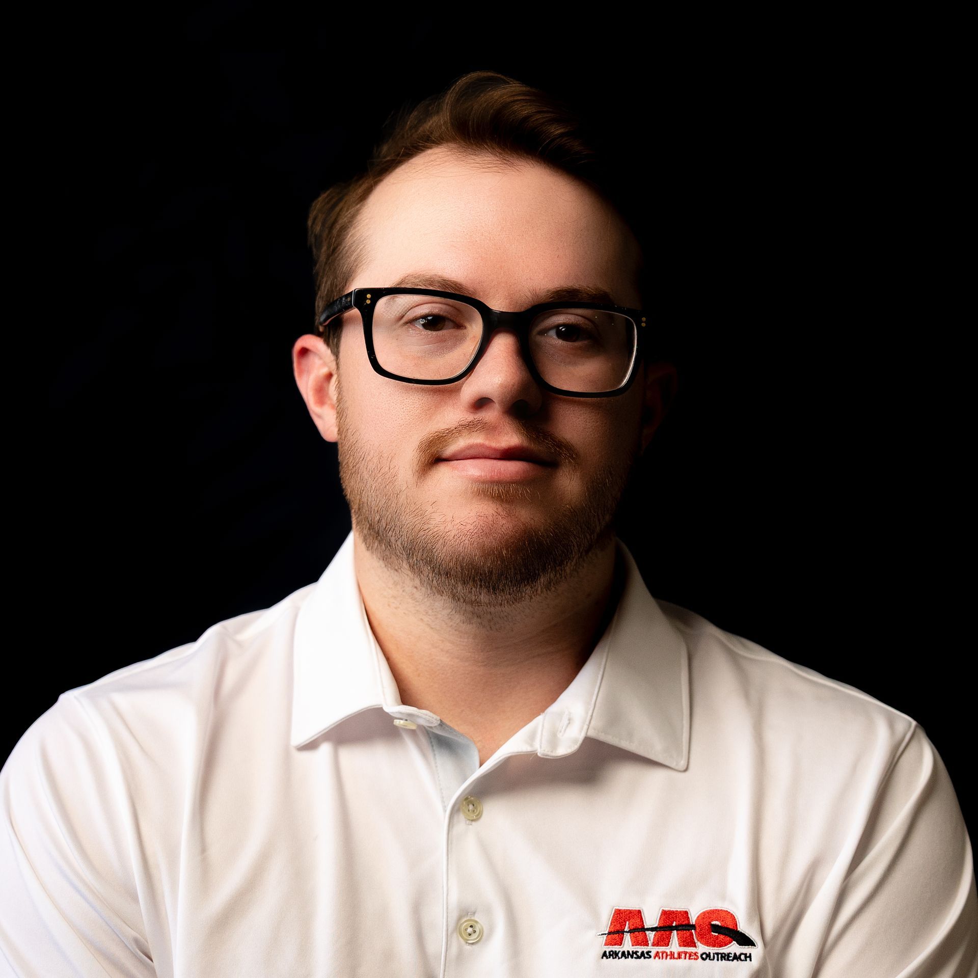 Portrait of a man in glasses wearing a white collared shirt against a black background